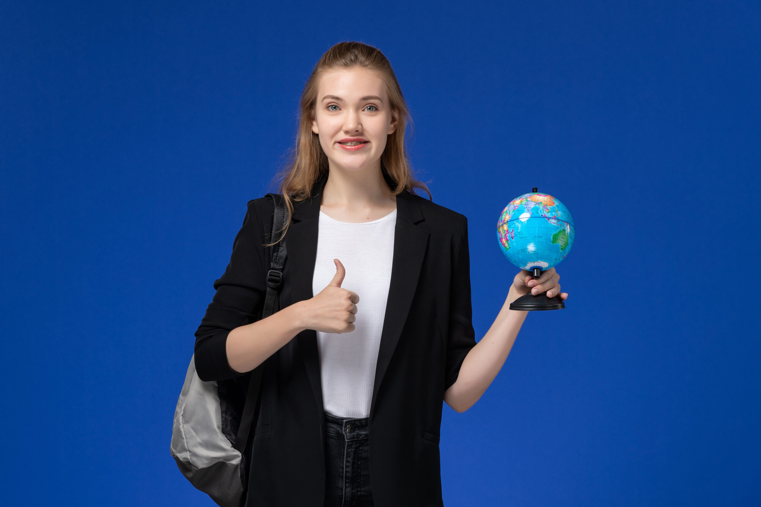 front-view-female-student-black-jacket-wearing-backpack-holding-little-globe-blue-wall-school-college-university-earth (1)
